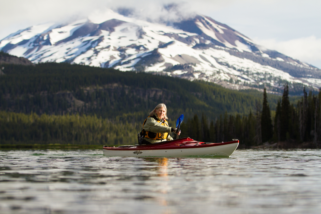 Woman paddling touring kayak with snow-capped mountain in background