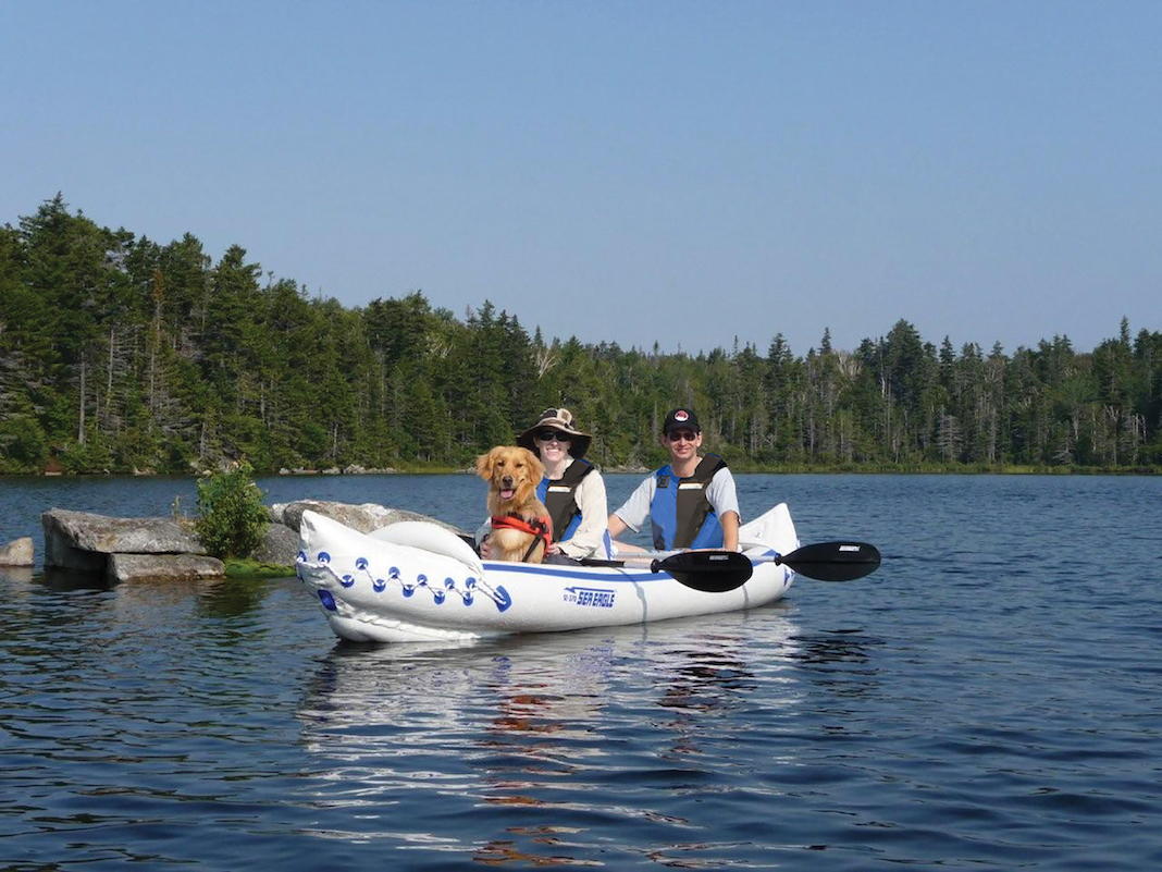 Man, woman, and dog in inflatable tandem kayak