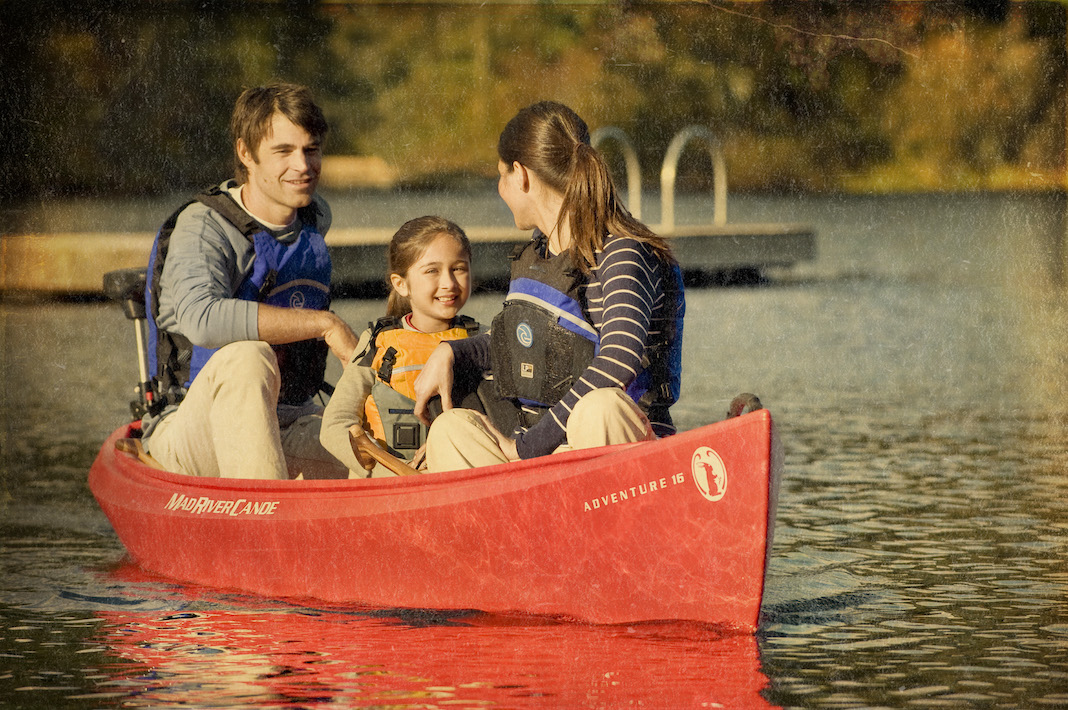 Two adults and child it in red canoes with dock in background.