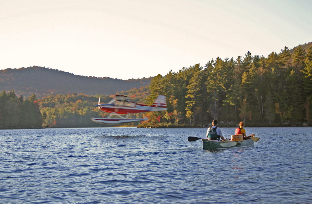 Two people floating in canoe on a lake as floatplane takes off.