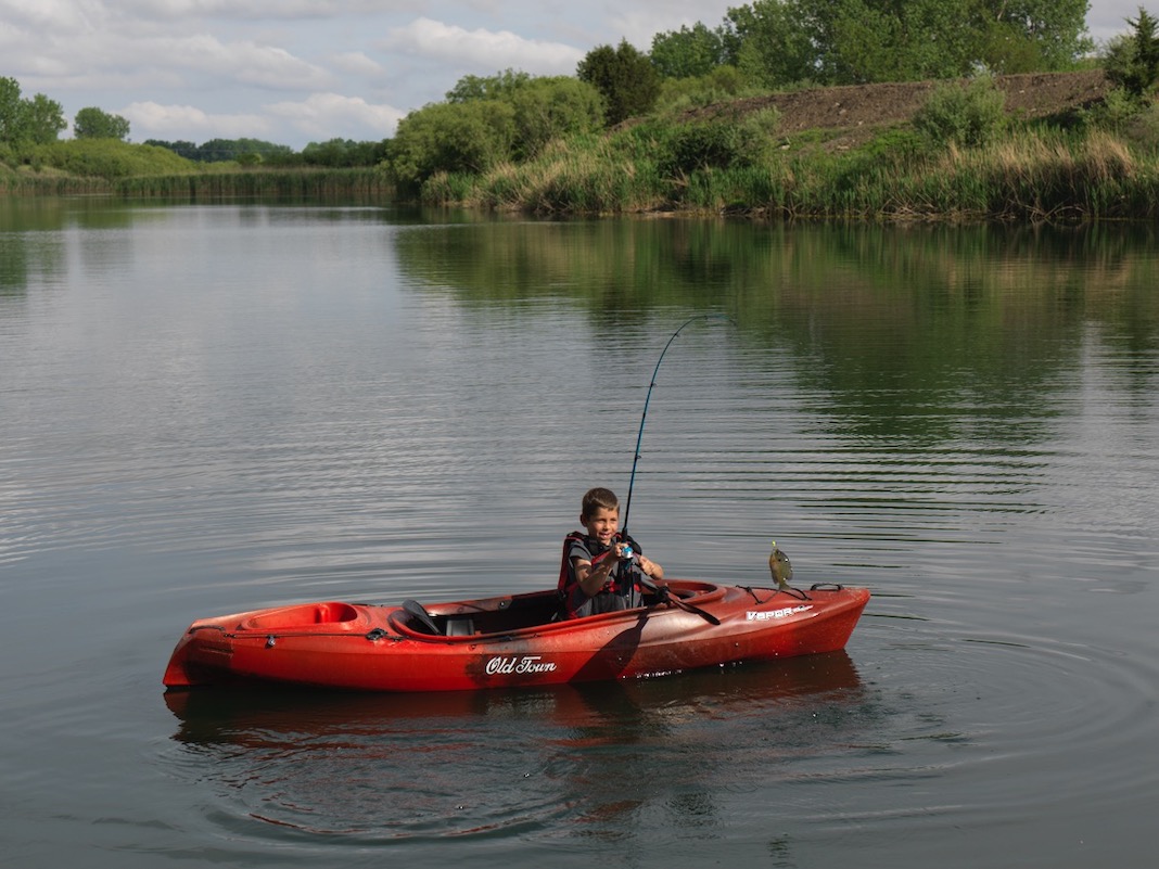 Boy fishing from red sit-inside kayak