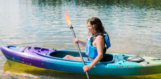 Woman paddling sit-inside green, blue and purple kayak