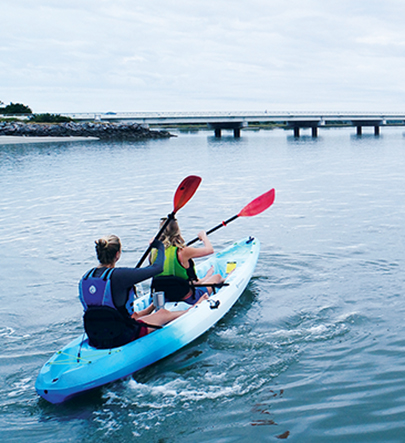 Two people paddling a tandem kayak towards a bridge