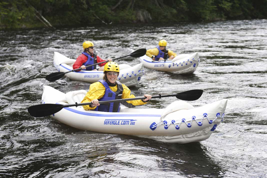 Three people paddling white inflatable kayaks and wearing helmets
