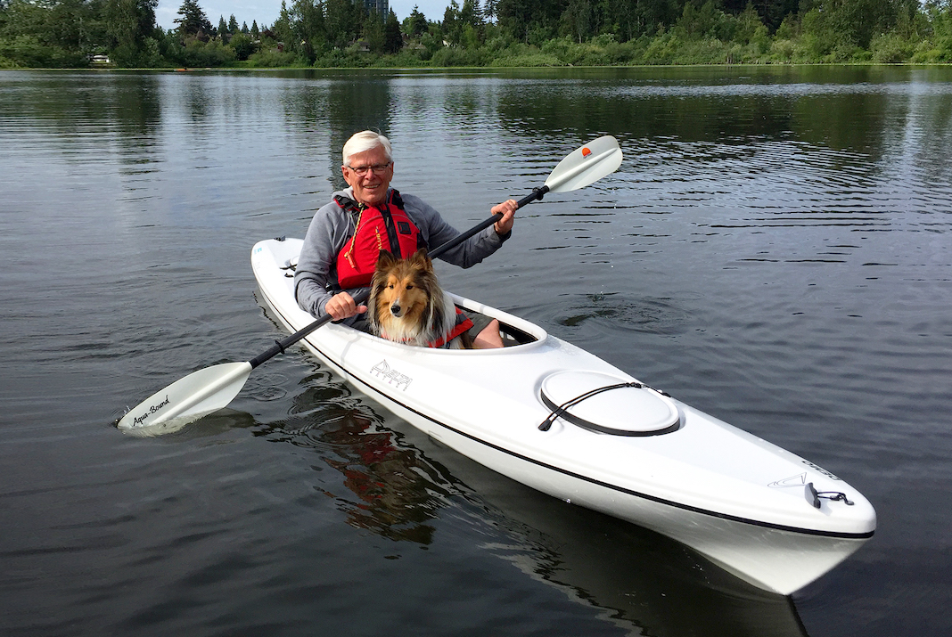 Man paddling white day touring kayak with dog in his lap