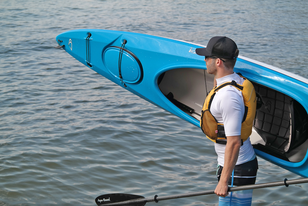 Man carrying blue day touring kayak on his shoulder