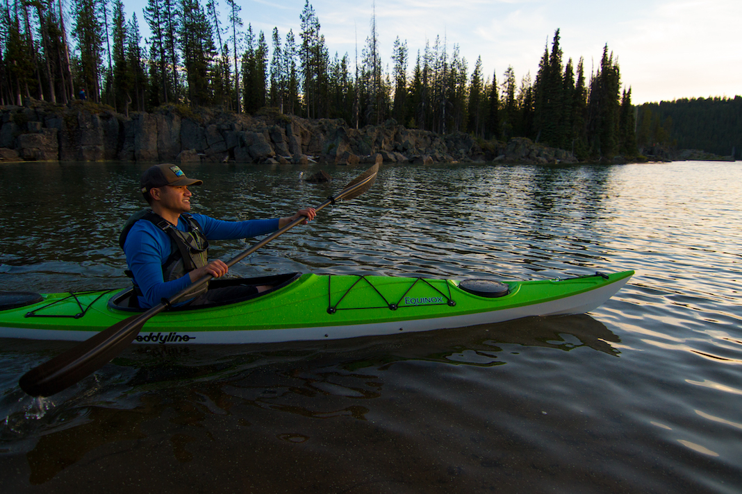 Man paddles green touring kayak at dusk
