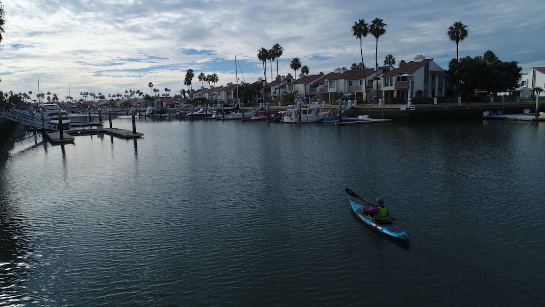 Person paddling kayak on calm waters with palm trees and houses in background
