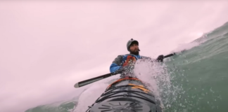 Sea kayaker leans into a brace as he surfs down the face of a wave
