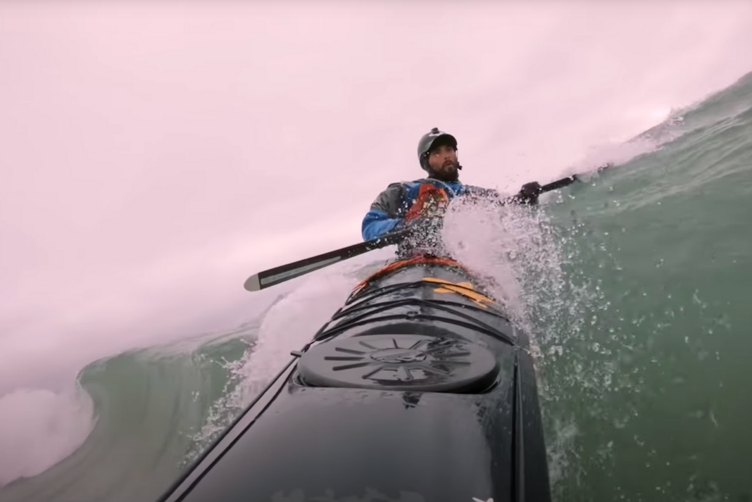 Sea kayaker leans into a brace as he surfs down the face of a wave