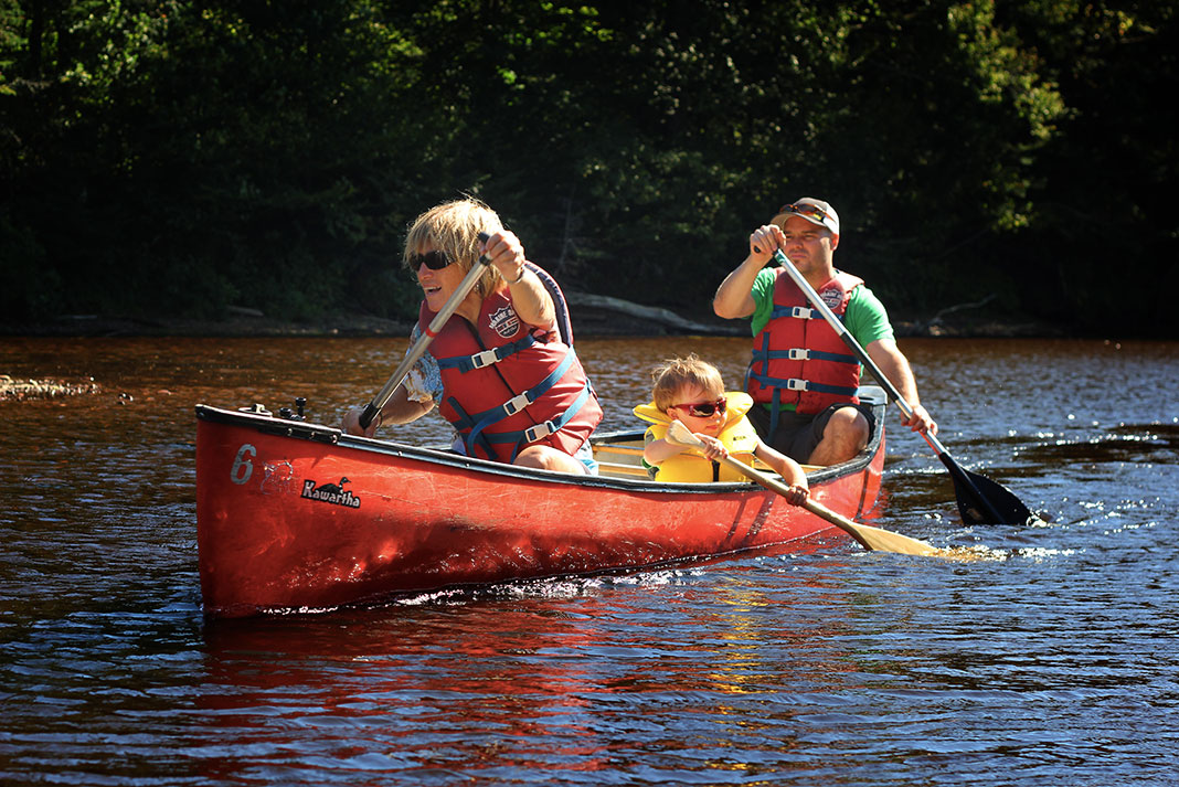 mother, father and young child canoe along a river in Quebec