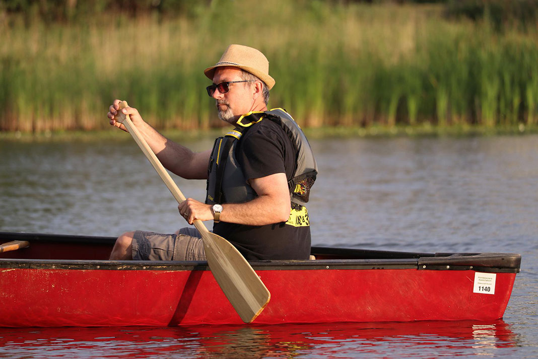 man paddles a canoe with a wooden canoe paddle