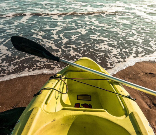 cheap yellow kayak and paddle sit on a beach at the water's edge
