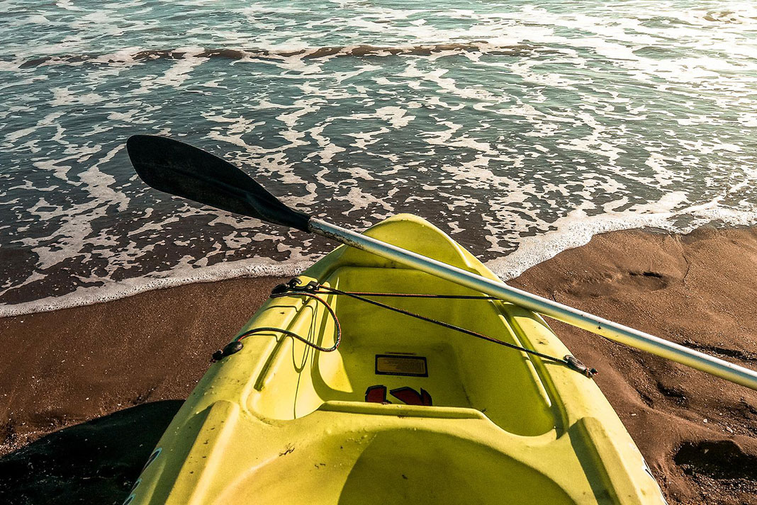 cheap yellow kayak and paddle sit on a beach at the water's edge