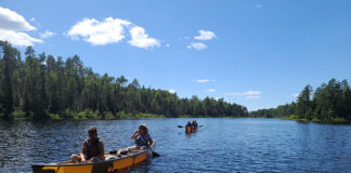 a group of people paddle in two lightweight Wenonah canoes on a guided canoe trip in Boundary Waters