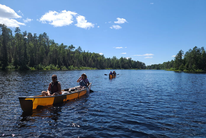 a group of people paddle in two lightweight Wenonah canoes on a guided canoe trip in Boundary Waters
