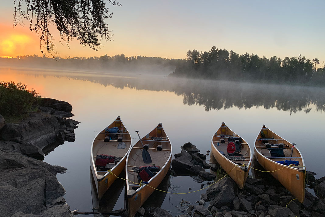 four canoes tied up on a glassy lake at dawn