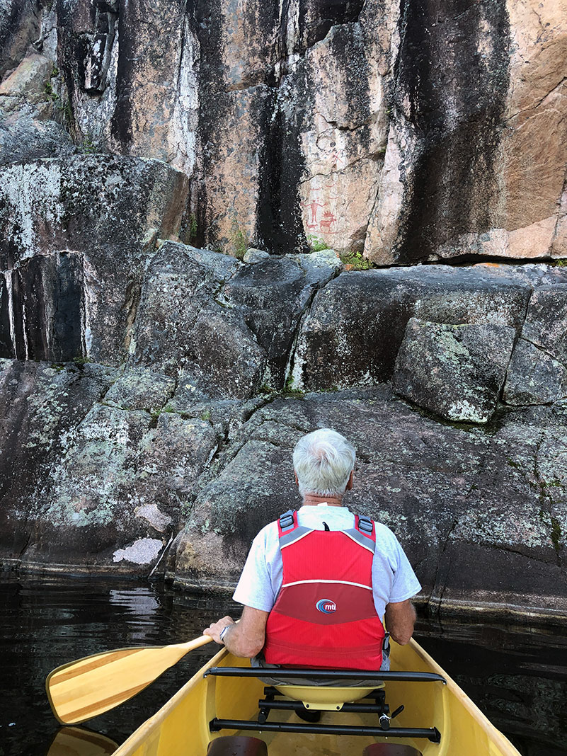 man with white hair sits in kayak and looks at Hegman Lake pictograph in Boundary Waters