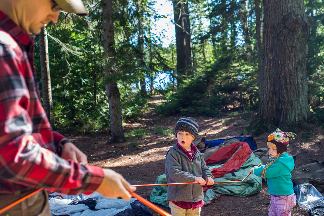 young boy and girl help their father set up a tent while on a camping trip