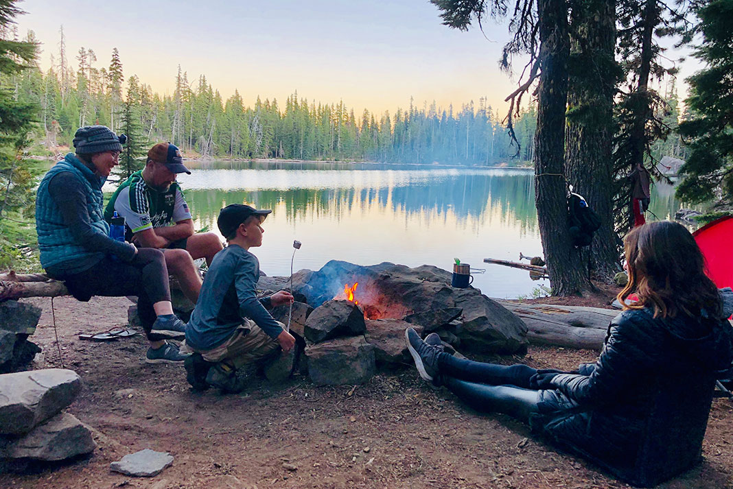 a family of campers sit around a campfire in front of a lake