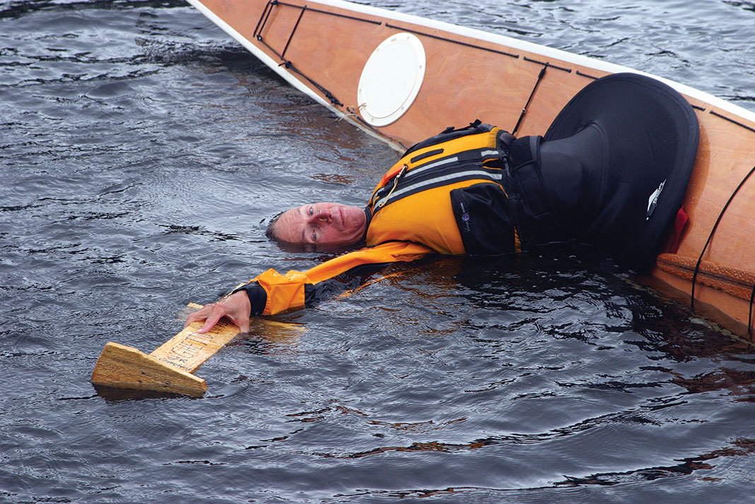 kayaker rolls his kayak while holding a wooden sculpture