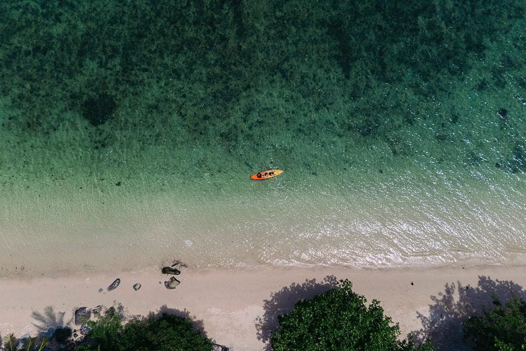 drone shot of an orange kayak paddling along a sandy beach in Fiji on the trip of a lifetime