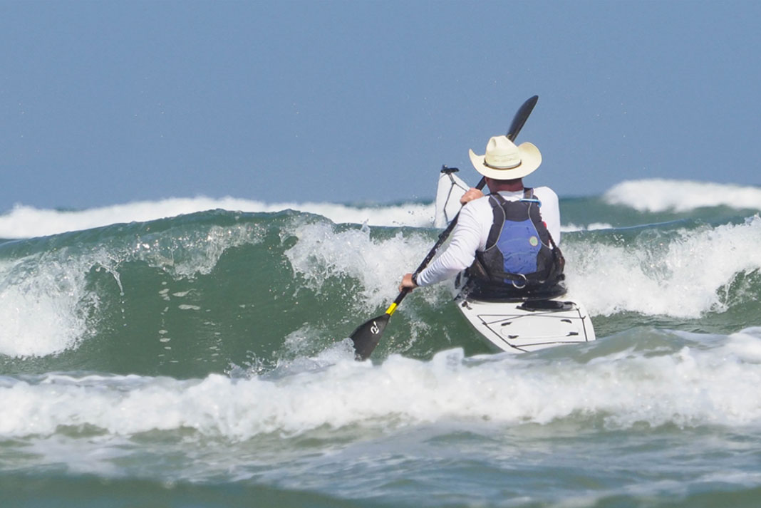 man paddles a kayak into the surf