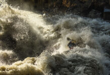 man kayaks through churning whitewater and spray