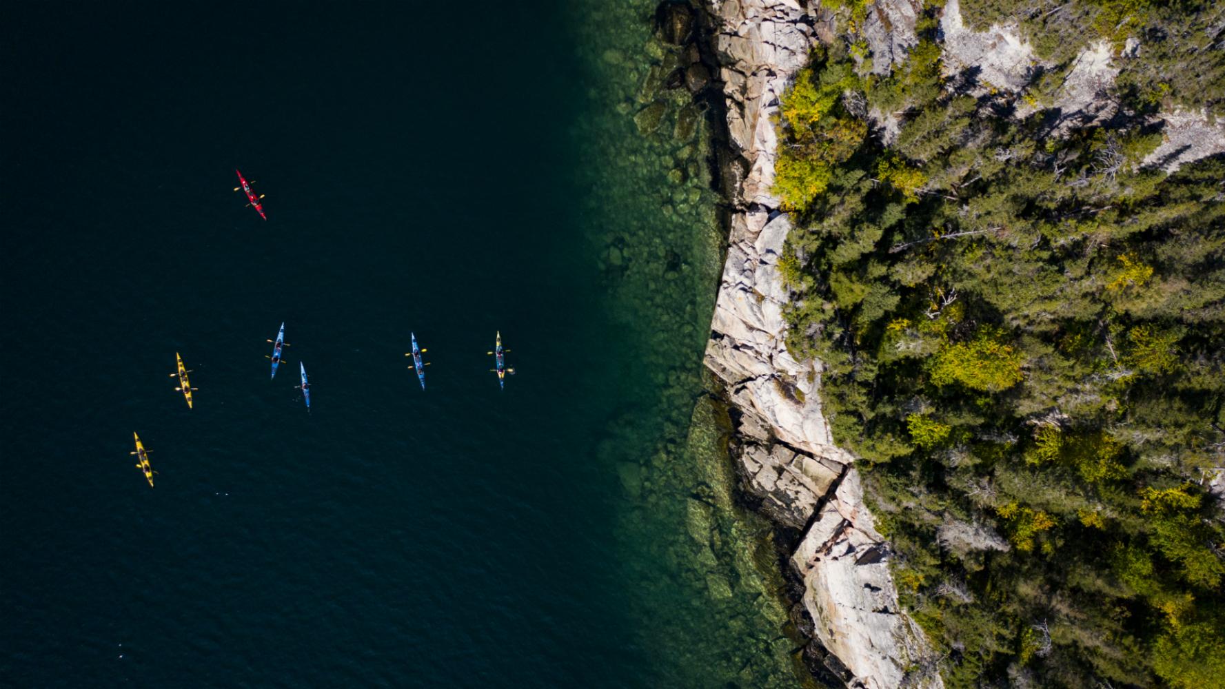 Overhead shot of tandem sea kayaks paddling along a rocky coast.