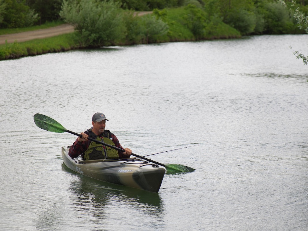 Older man paddling green sit-inside fishing kayak