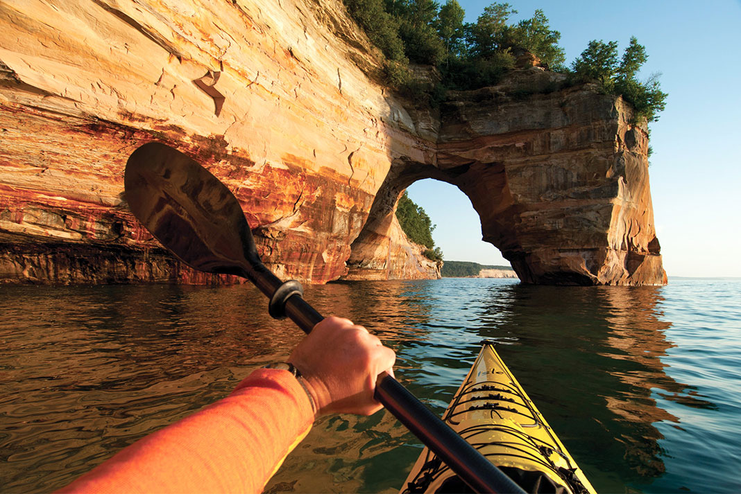 Photo from point of view from kayaker in a sea kayak, paddling towards rock arch.
