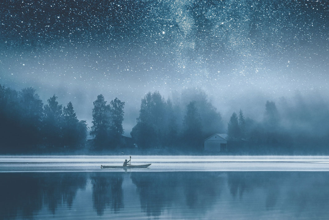 sea kayaker paddles on a still lake under a starry sky