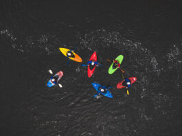 overhead photo of a group of colorful whitewater kayakers on black water