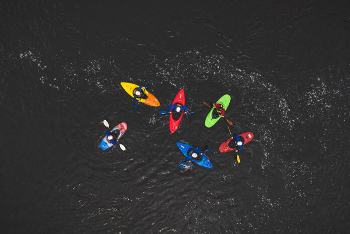 overhead photo of a group of colorful whitewater kayakers on black water