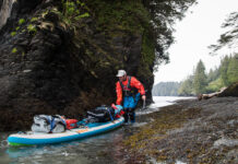 man pushes a paddleboard loaded down with backcountry paddling gear