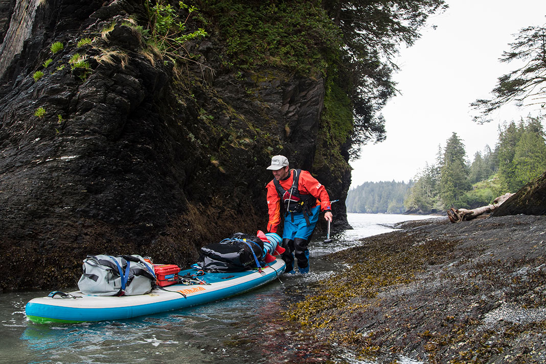 man pushes a paddleboard loaded down with backcountry paddling gear