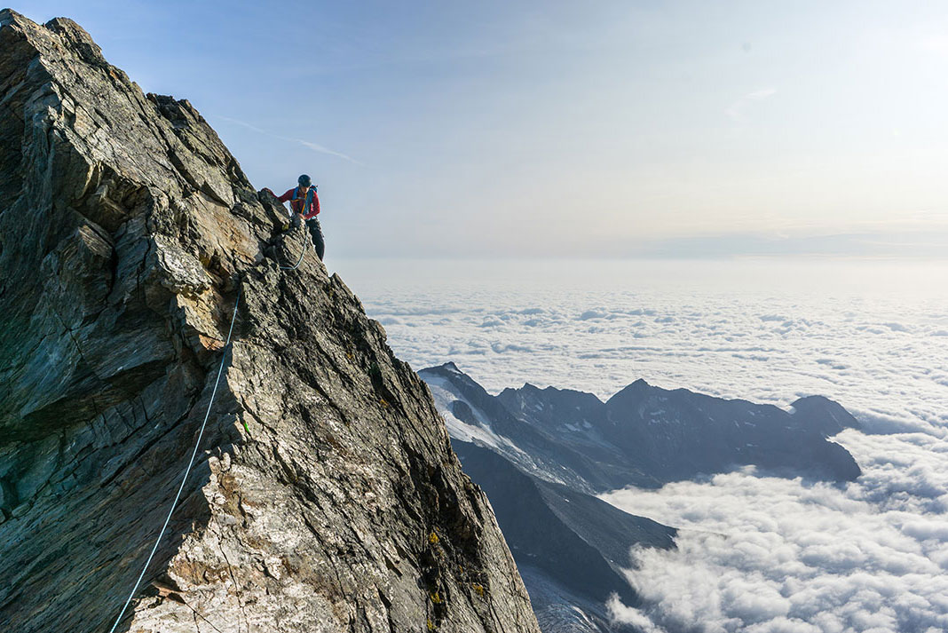 person climbing a mountain above the clouds