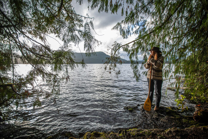 Dianne Whelan stands at the water's edge holding a paddle