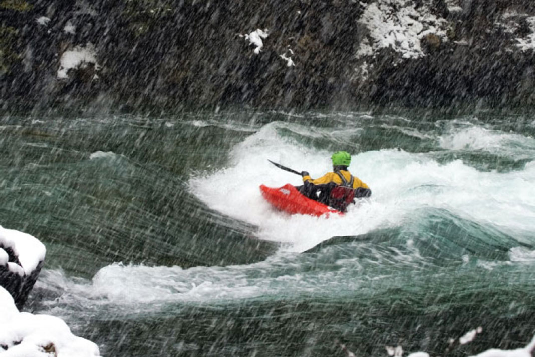 person whitewater kayaking in a snow squall