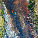 30 Essential River Running Skills overhead photo of red and blue kayaks running a rocky river
