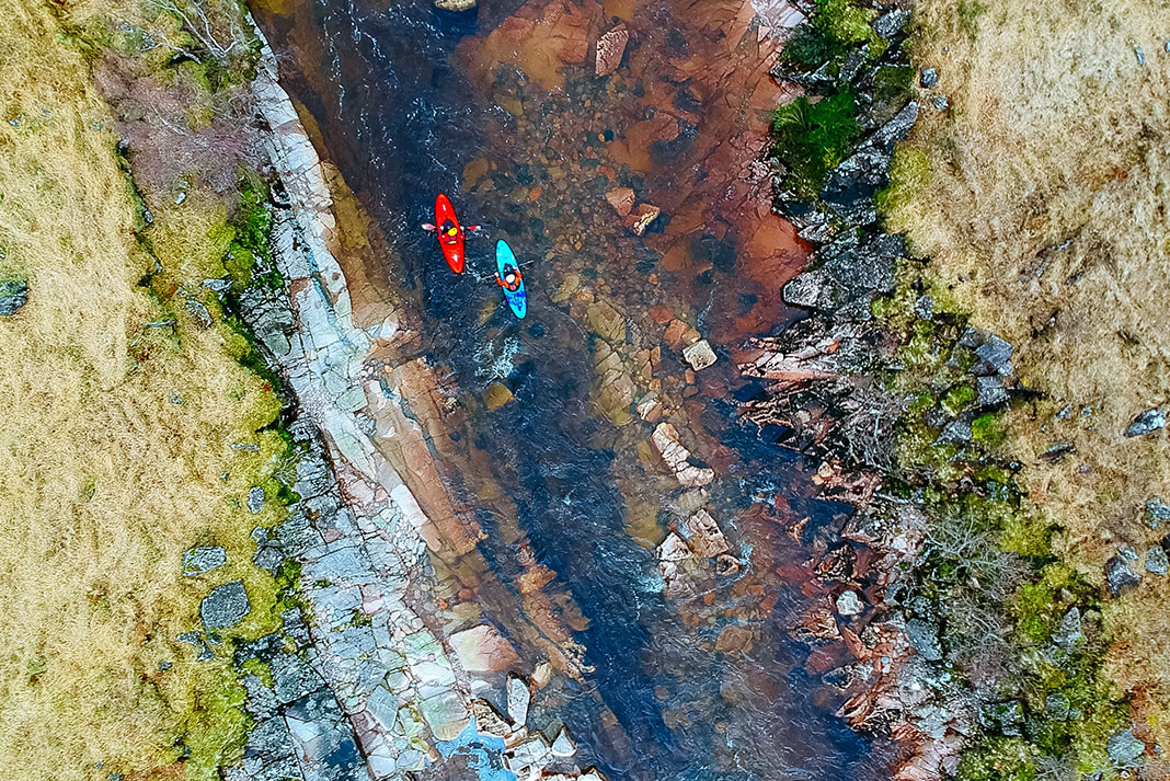 overhead photo of red and blue kayaks running a rocky river