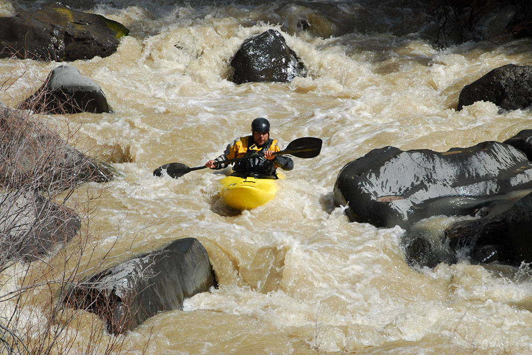 man running a rocky brown river in a yellow kayak
