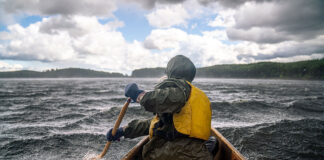 person in rain gear paddles a canoe across a choppy lake