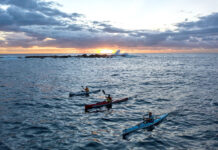 three sea kayakers paddle across the Bass Strait at dusk