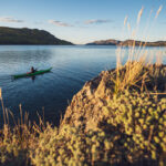 Skeg Vs Rudder: The Great Kayak Debate kayaker paddles past a grassy knoll
