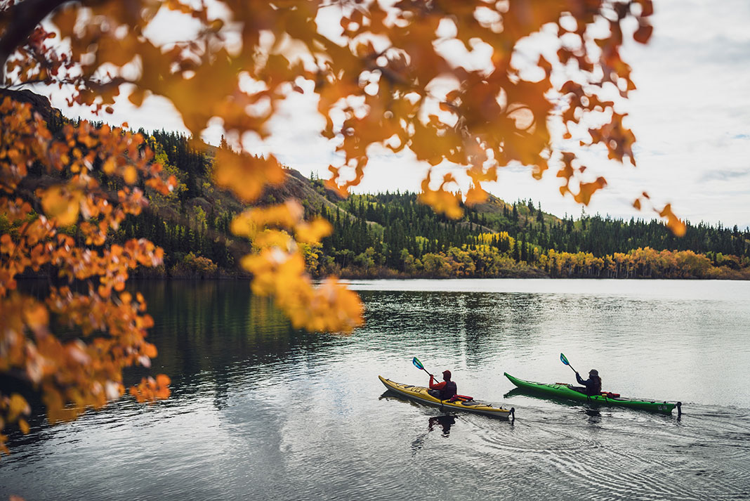 two kayakers paddling touring kayaks with rudders with fall foliage in the foreground