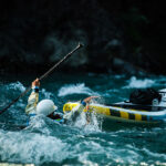 SUP Leashes: Explaining The Most Controversial Piece of River Gear man swims in whitewater beside a paddleboard connected to him with a SUP leash