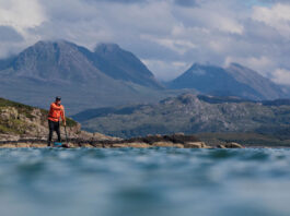paddleboarder stands in front of mountain landscape while he circumnavigates Great Britain