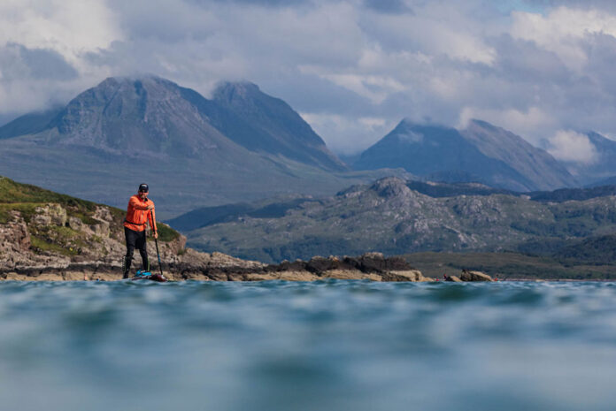 paddleboarder stands in front of mountain landscape while he circumnavigates Great Britain
