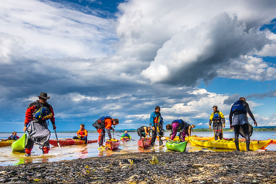 a group of kayakers with colorful boats and apparel gather near shore